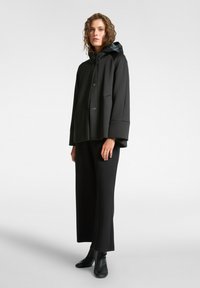 Czarny, oversize'owy płaszcz z kapturem o gładkiej fakturze, z dwoma dużymi guzikami z przodu. Noszony na czarne, szerokie spodnie i botki do kostki w tym samym kolorze.