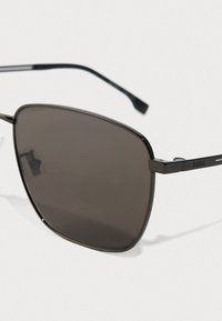 Artimas juodų metalinių rėmelių akinių su tamsiais stačiakampiais lęšiais ir "BOSS" logotipu ant šoninės juostos vaizdas, esančio balto fono.