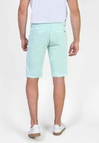 Mintgroene shorts van katoen, tot halverwege de dijen, met een gladde textuur en twee achterzakken. Gecombineerd met witte sneakers.