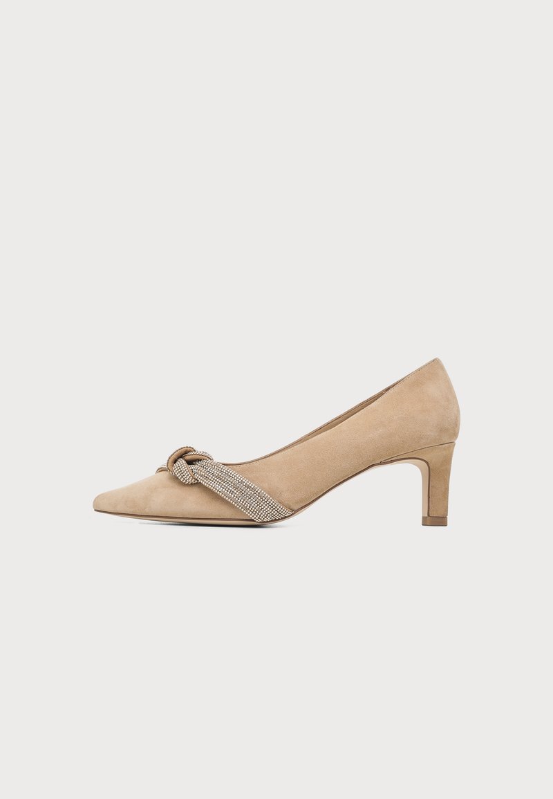 Escarpin beige en daim à talon moyen, bout pointu et bride nouée ornée de strass sur le devant.