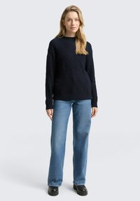 Granatowy sweter w splot żakardowy z wzorem diamentowym, w połączeniu z jasnoniebieskimi dżinsami o prostym kroju i czarnymi botkami na platformie.