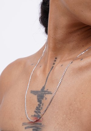 Silver chain necklace with a flat, smooth design and intricate links, draping elegantly over skin with visible tattoos.