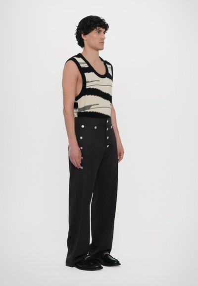 Top de malha em creme com padrão abstrato preto, combinado com calças escuras de cintura alta com botões prateados e corte reto.