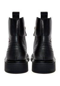 Paire de bottines en cuir noir avec des détails cousus, des languettes à l'arrière et des semelles plates à plateforme, vues de dos.