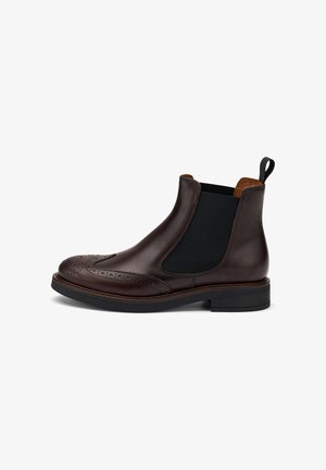 Stivaletto Chelsea in pelle marrone con dettagli brogue, pannelli laterali elastici e un anello per il tiraggio. Suola spessa con un leggero tacco. Finitura liscia.