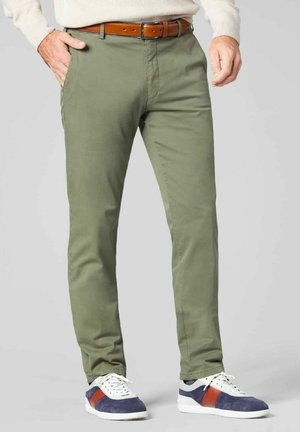 Chino olive avec une coupe slim, présentant une texture lisse, des poches avant et une ceinture en cuir marron. Associé à des baskets blanches et marines.