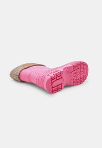 Barna filc felsőrész, pink gumitalppal, amely texturált tapadási mintával rendelkezik és állítható pánttal van ellátva a megfelelő illeszkedés érdekében.