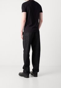 Černé tričko s krátkým rukávem v kombinaci se volnými tmavými džínovými kalhotami s bočními kapsami a kontrastním šitím. Oblečení doplňují černé boty.