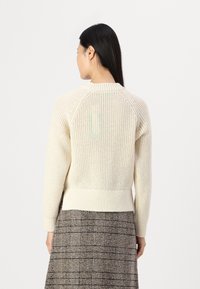 Maglione lavorato a maglia color crema con orlo e polsini a coste, caratterizzato da un motivo testurizzato, maniche raglan e un design con schiena scoperta.