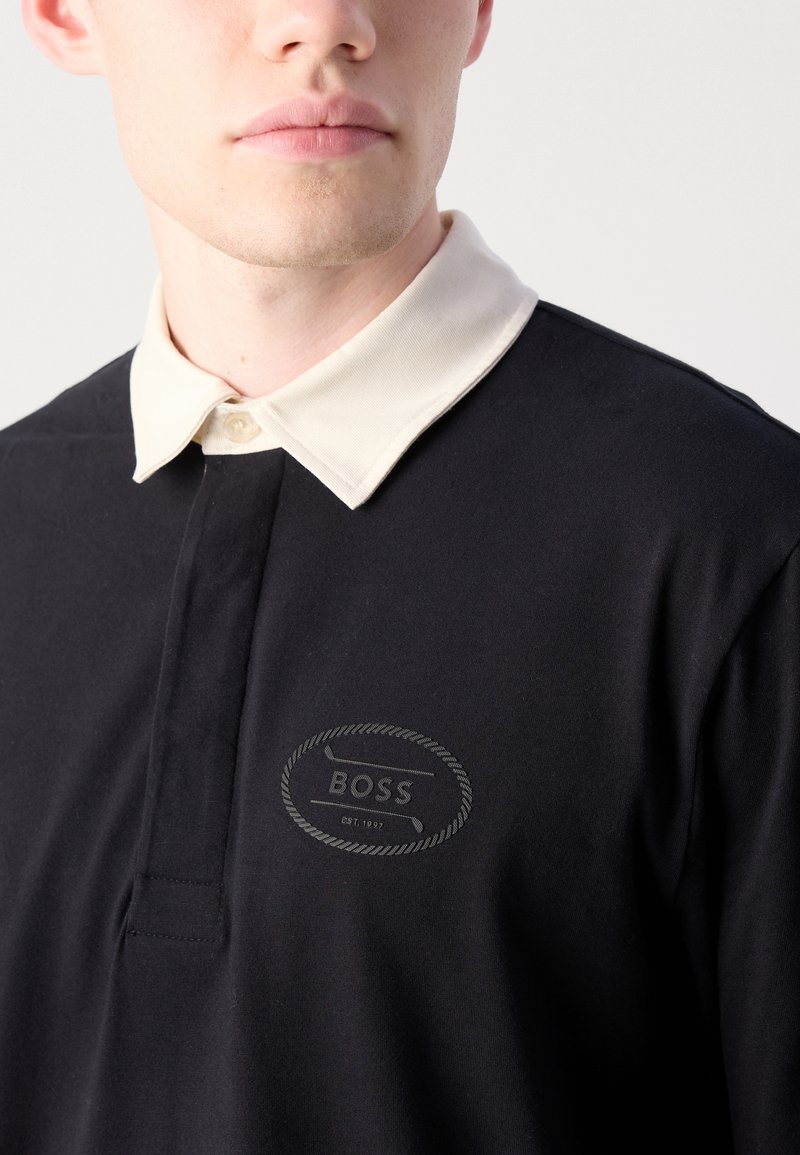 Zwarte polo met een contrasterende crèmekleurige kraag, voorzien van een gestikt logo in een ronde vorm. Zachte stof met een gladde textuur.