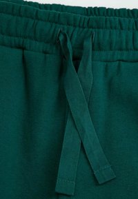 Zielone bawełniane szorty z elastyczną talią i sznurkiem. Materiał ma gładką fakturę i jest jednolity, bez wzorów.