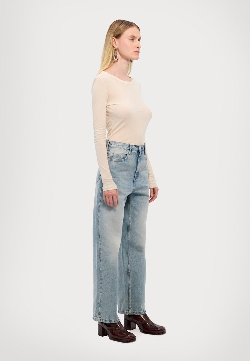Beige long-sleeve top, light-wash wide-leg jeans, and glossy brown block-heeled shoes, showcasing a relaxed fit and casual style.