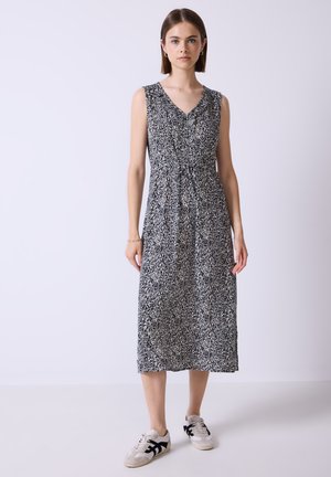 Ärmelloses schwarz-weißes Blumenkleid in Midi-Länge mit V-Ausschnitt, gerafftem Bund und leichtem Stoff. Kombiniert mit lässigen Sneakers.