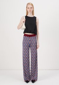 Top corto nero senza maniche con una vestibilità ampia, abbinato a pantaloni larghi a fantasia che presentano forme geometriche in rosso, blu e bianco.
