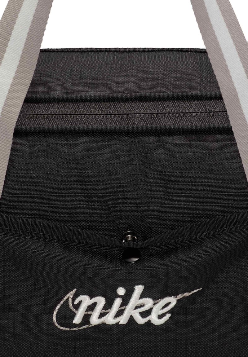 Bolsa de tela negra con correas grises, que cuenta con un cierre de cordón y un logotipo de "Nike" bordado en blanco en la parte frontal.