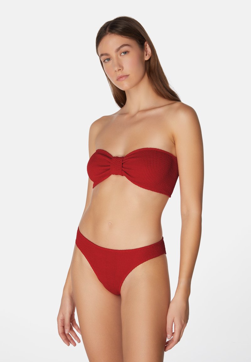 Röd ribbad bikini-set bestående av en bandeau-topp med en knuten detalj och högskurna bottnar, båda med en mjuk textur och sömlös design.