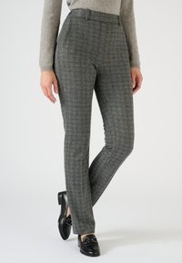 Grijze broek in een visgraatpatroon met een getailleerde fit, voorzien van twee zijzakken en een vlakke voorkant. Gecombineerd met zwarte loafers.