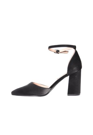 Scarpa con tacco alto in camoscio nero, punta appuntita, tacco a blocco e cinturino alla caviglia con fibbia, vista laterale su sfondo bianco.