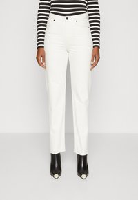 Hvite jeans med rett passform, som har råkant. Sammen med svarte spissede ankelstøvler og en svart-hvitstripete topp.