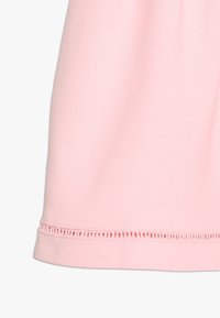 Tissu en coton rose clair, texture lisse, comportant un ourlet décoratif avec un motif cousu et un drapé doux et fluide.