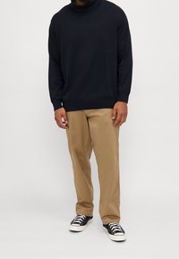 Marinefarbener Rollkragenpullover mit langen Ärmeln, kombiniert mit beigen Hosen und schwarzen Low-Top-Sneakern mit weißen Sohlen und Schnürsenkeln.