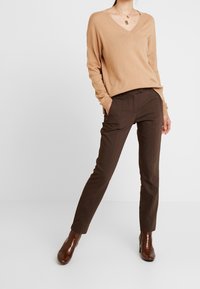 Beige V-ringad tröja med långa ärmar, ihop med bruna skräddarsydda byxor. Bruna klackade ankelskor. Enkel, mjuk textur.