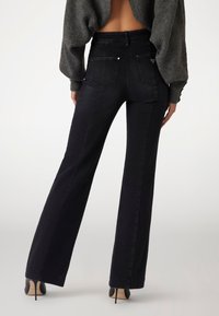 Black high-waisted jeans with a fitted silhouette and flared legs, featuring back pockets and a minimalistic design.