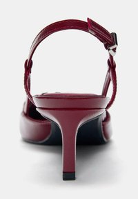 Escarpin en cuir rouge à talon moyen étroit et bride à boucle ajustable, présenté de dos sur fond blanc.