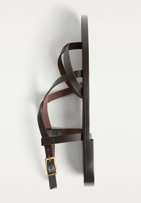 Brun lædersandal med krydsende stropper, flad sål og en metal spænde accent. Sideprofilbillede, der fremhæver enkelheden i designet.