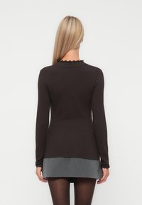 Top marrone a maniche lunghe con texture a coste e dettagli arricciati sul collo, abbinato a una gonna grigia. La vista laterale e quella posteriore mostrano una silhouette aderente.