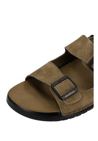 Braune Wildleder-Sandale mit zwei verstellbaren schwarzen Schnallen, offenem Zehenbereich und schwarzer Gummisohle, vorne an der Schnalle mit "wojas"-Logo versehen.