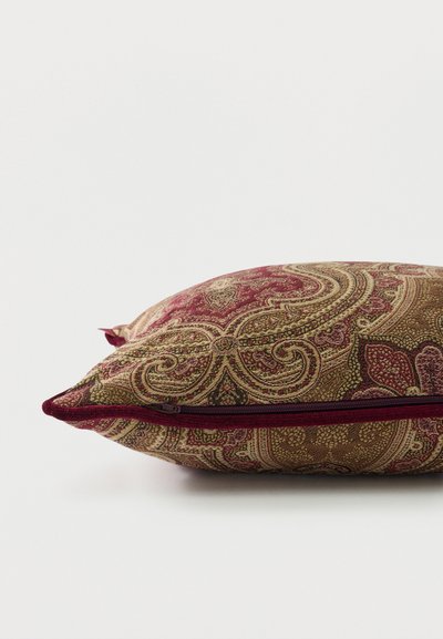 Coussin rectangulaire avec un motif cachemire complexe en tons dorés et bordeaux, présentant une fermeture éclair bordeaux visible le long d'un bord.