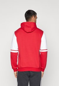 Röd och vit hoodies med lång ärm, justerbar huva och ribbade ärmslut. Har kontrasterande ränder på armarna och ryggen.