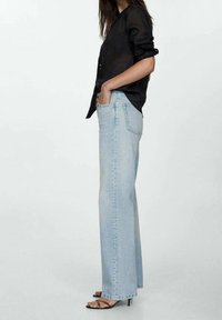 Jeans de pierna recta en azul claro, fabricados en denim, con una cintura alta y diseño tradicional de cinco bolsillos. Combinados con una camisa negra de botones.