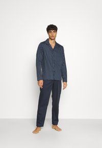 Set di pigiama a righe blu navy con maniche lunghe e chiusura con bottoni, caratterizzato da pantaloni scuri e una vestibilità comoda. Tessuto dalla trama liscia.