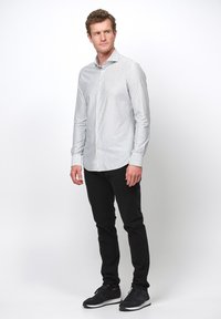 Wit en grijs gestreept overhemd met lange mouwen, slim fit, met een knoopjeshals, gecombineerd met zwarte broek en zwarte sportschoenen.