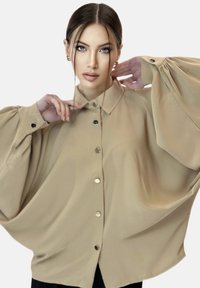 Beige oversized shirt gemaakt van gladde stof, met een klassieke kraag, knoopsluiting aan de voorkant en volumineuze mouwen met manchet details.
