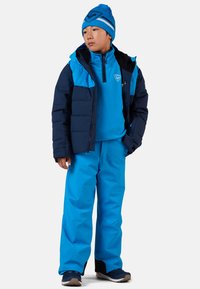 Giacca imbottita blu con un'intercapedine di pile blu a contrasto, pantaloni da neve blu e un berretto di lana abbinato. Presenta zip e loghi.