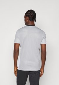 Γκρι αθλητικό μπλουζάκι με κοντά μανίκια, πλέγμα υφής, μαύρες λεπτομέρειες και στρογγυλή λαιμόκοψη. Παρουσιάζει αθλητικό σχέδιο με πλευρικά πάνελ.