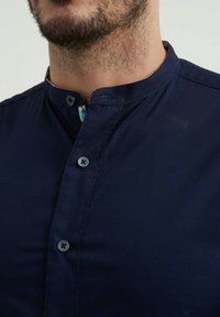Chemise bleu marine à manches courtes avec un col bandé, dotée de deux fermetures à boutons et d'une texture subtile. L'intérieur du col présente un motif.