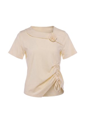 Beige short-sleeve top with an asymmetrical collar, fabric rose detail, and side ruching with ties on a plain background.