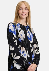 Blumenkleid mit schwarzem Hintergrund, blauen und beigen Blumenmustern, langen Ärmeln und einem plissierten Design für Textur.