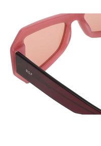 Occhiali da sole esagonali con montatura rosa traslucida, lenti oscurate e lati neri caratterizzati da una discreta scritta sulla asta.