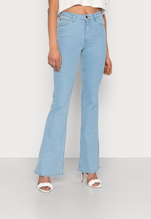 Ljusblå utsvängda jeans i denim. Har hög midja och lätt slitning, ihop med vita klacksandaler.