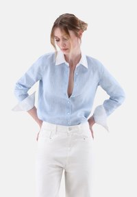 Light blue striped shirt with white collar and cuffs, button-down front, relaxed fit, paired with white high-waisted trousers.