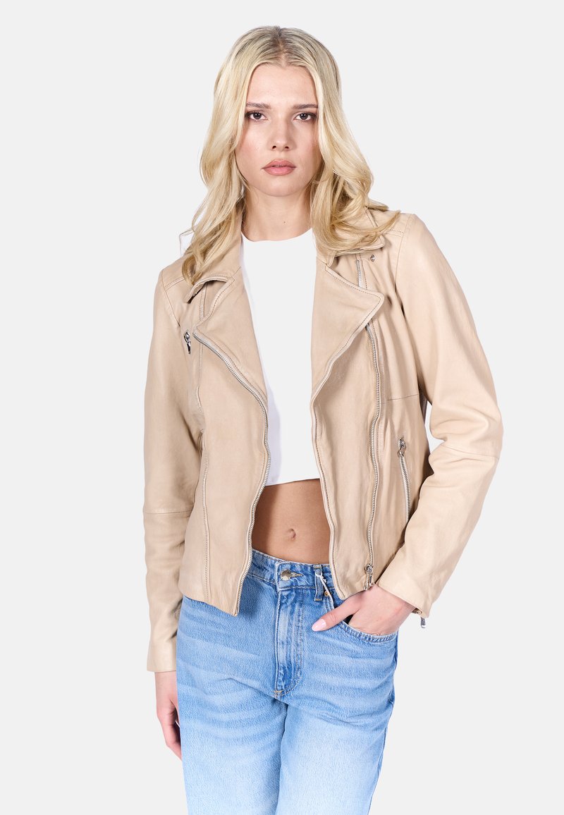 Beige leren motorjack met een asymmetrische rits, ritszakken en een getailleerde pasvorm, gedragen over een cropped witte top en lichtblauwe spijkerbroek.