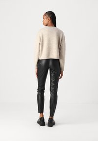 Beige cropped trui met lange mouwen, gecombineerd met strakke zwarte leren broek. Glad textuur en subtiel breipatroon zichtbaar.