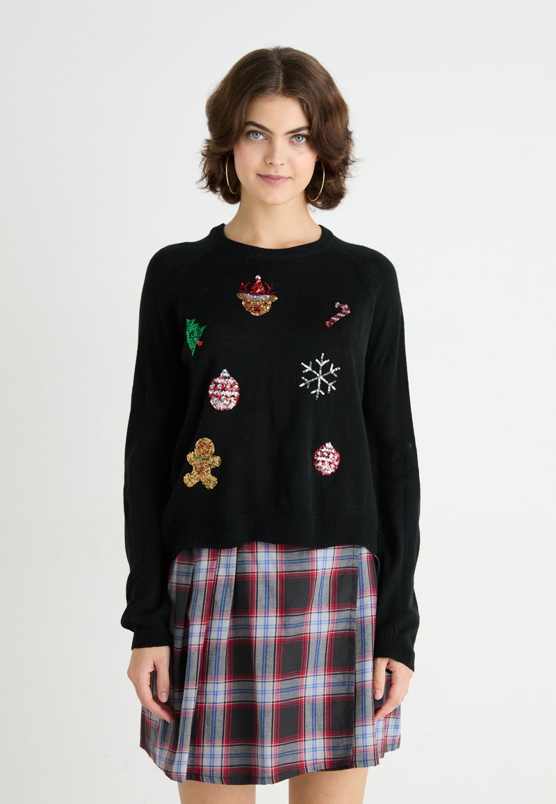 Pulover negru cu aplicații festive colorate, inclusiv ornamente, fulgi de zăpadă, turtă dulce și un brad de Crăciun. Guler și manșete striate.