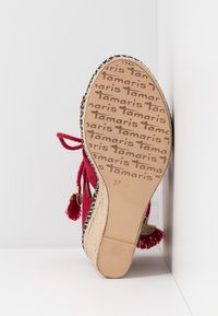 Semelle d'une sandale compensée rouge avec plateforme en jute tressé, motif marqué "Tamaris" sur la semelle, pompons rouges et taille 37 embossée au fond.