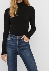 Jersey negro de cuello alto con mangas largas, diseño ajustado, hecho de material suave. Combinado con jeans ajustados azul oscuro, con un detalle mínimo.